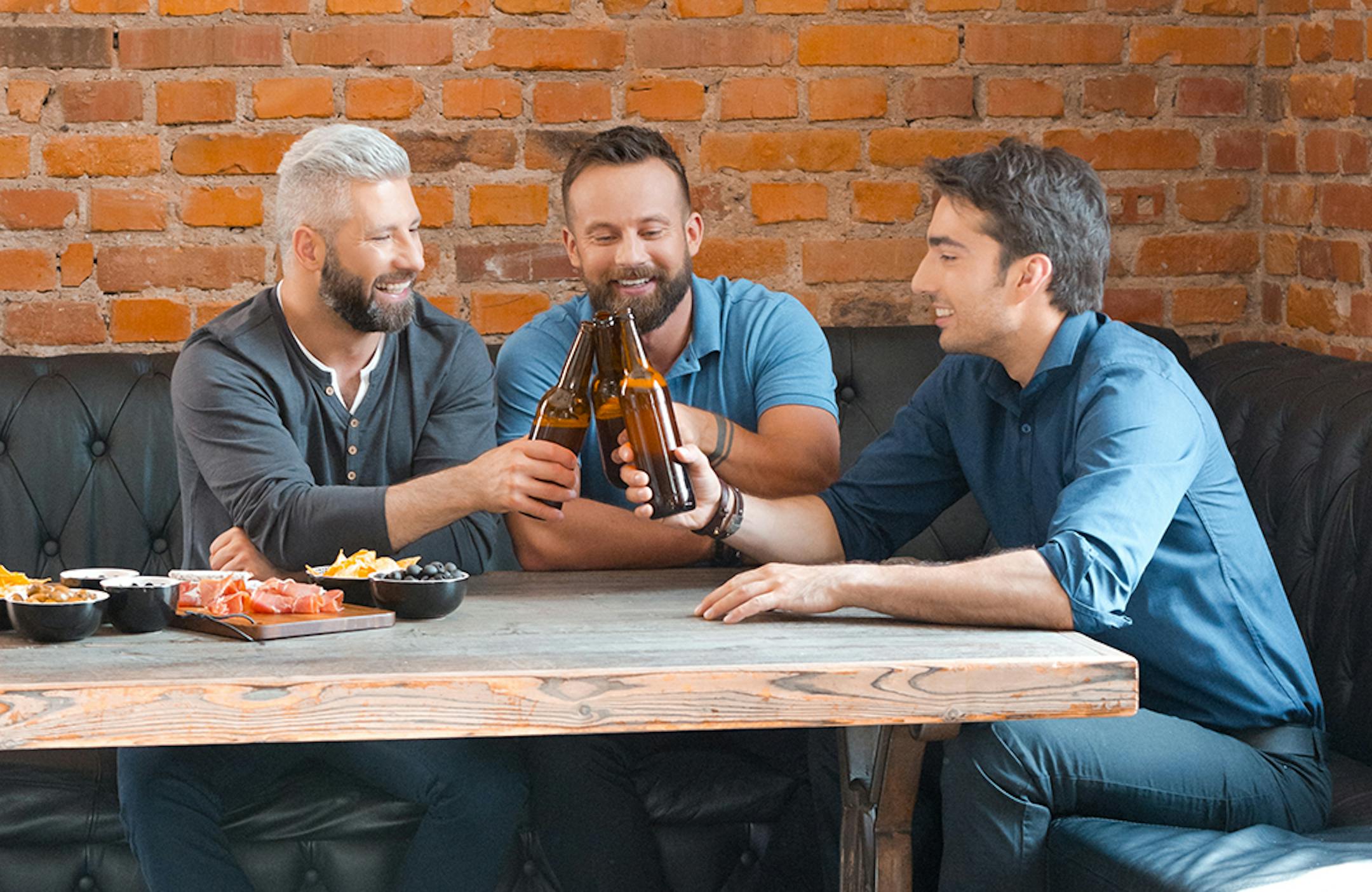 Three friends toasting with beer bottles in the pub. Happy friends meeting after work and having beers.