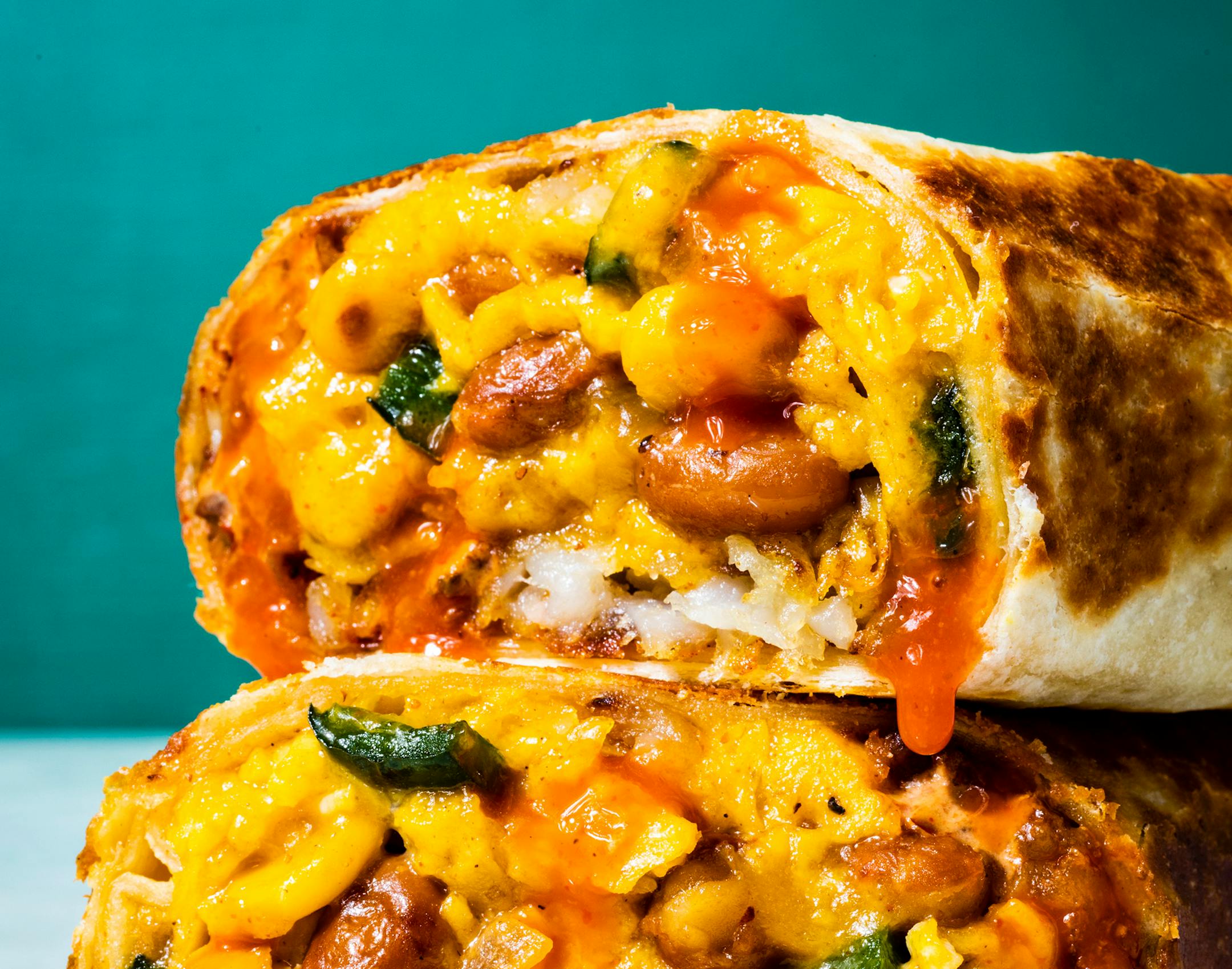 A close-up picture of a breakfast burrito with poblano, beans, corn and crispy potatoes with a chipotle sour cream.