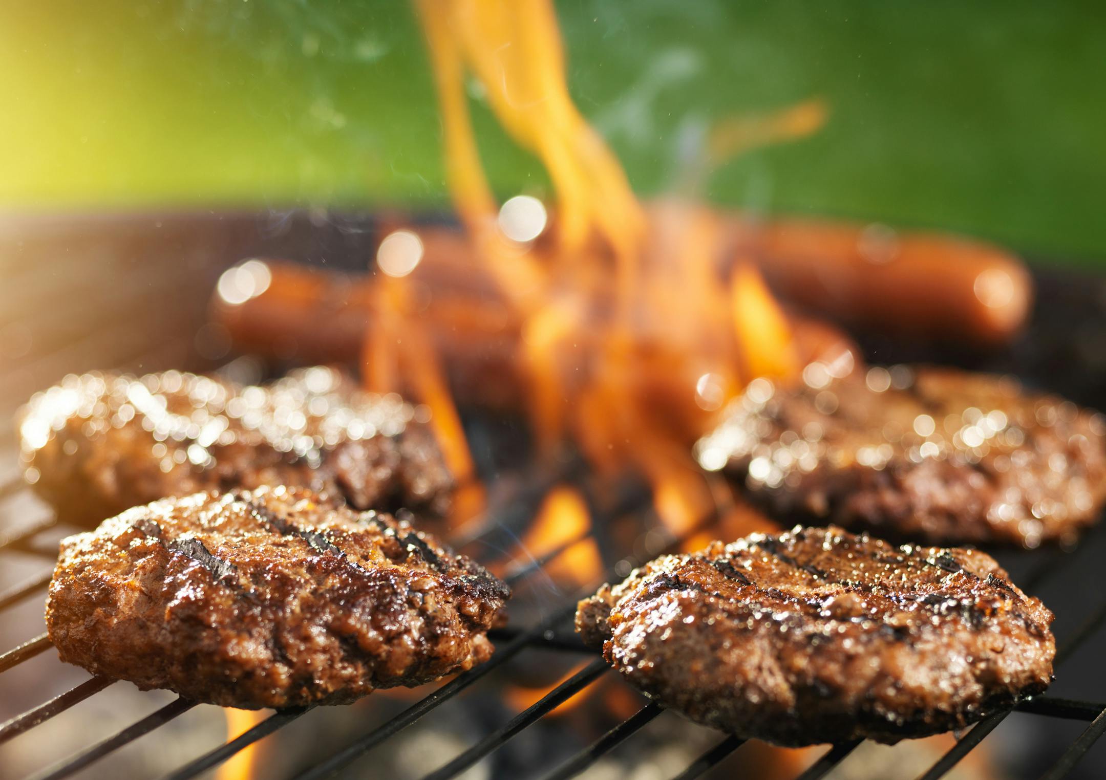 hamburgers and hotdogs cooking on flaming grill shot with selective focus