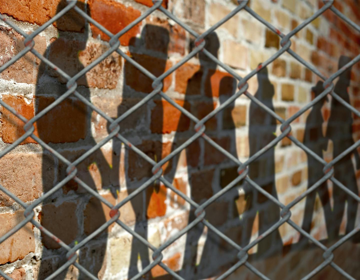 Shadows of people on a wall behind a fence