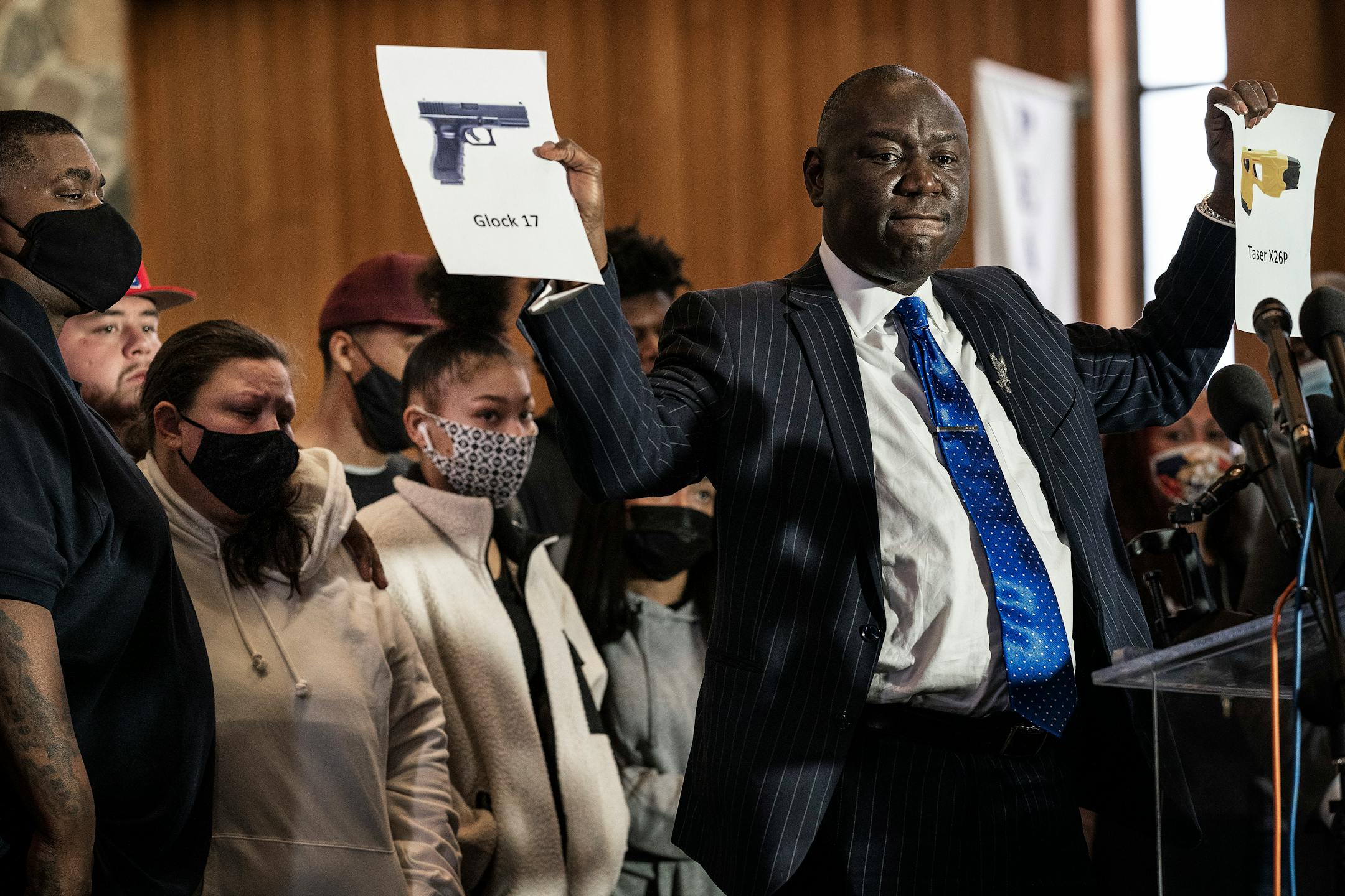 Family of Daunte Wright watched as attorney Ben Crump held up photos of a Glock 17 pistol  nd a Taser X26p during a news conference In Minneapolis.
