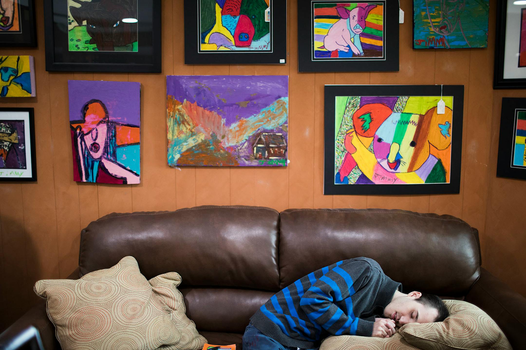 Jimmy Reagan sits on a couch below some of his artwork on display at Sunfish Cellars Wine & Spirits in St. Paul.