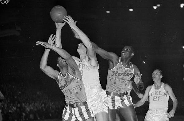 Minneapolis Lakers' George Mikan grabs a rebound in front of Harlem Globetrotters players Nat "Sweetwater" Clifton, left, and Babe Pressley during a b