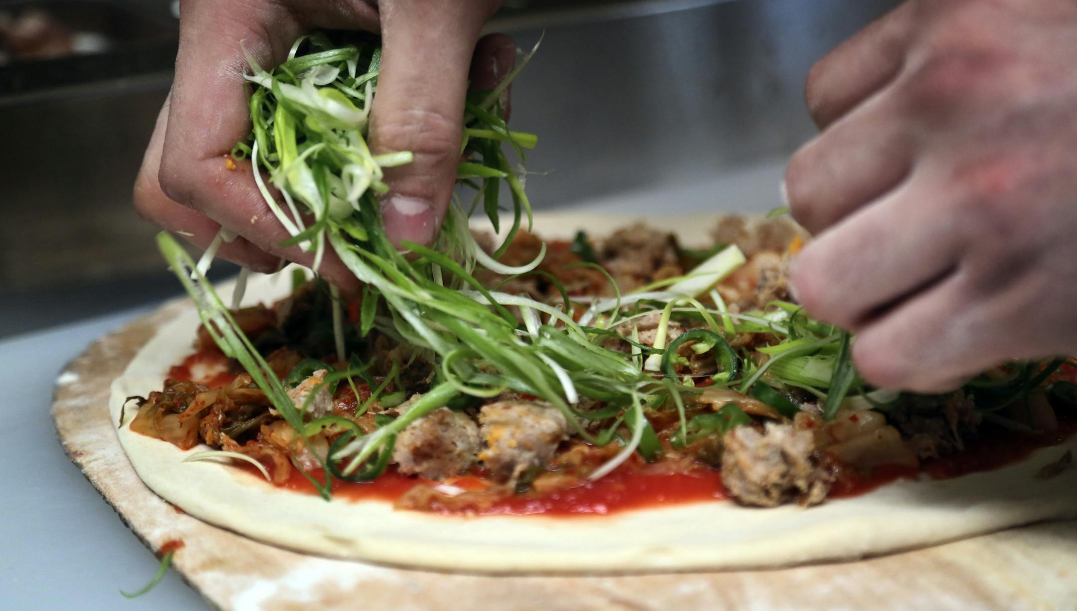 At Pizzeria Lola, pizza chef Bishara Sahoury adds fresh scallions to the Lady Za Za pizza -- a kim chi based pizza made with Italian red sauce, house-made kimchi, Korean sausage, serrano peppers, scallions and sesame and soy chilli glaze Friday, April 11, 2014, in Minneapolis, MN.]](DAVID JOLES/STARTRIBUNE) djoles@startribune.com Story on the popularity of a Korean cabbage food - from gourmet pizza to a general mills product - owner Ann Kim offers a pizza made with it.**Bishara Sahoury,cq