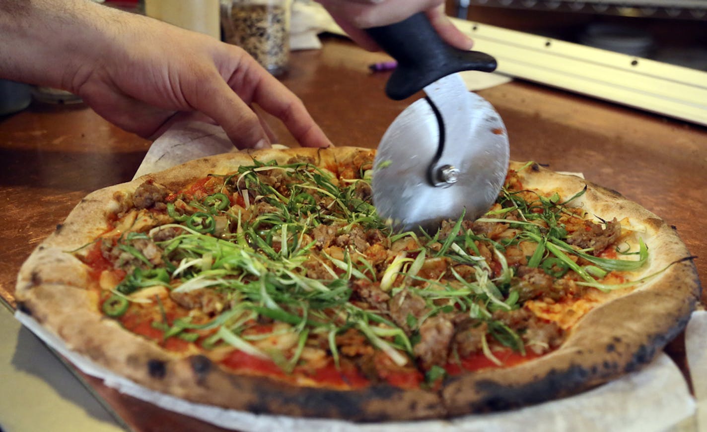 At Pizzeria Lola, pizza chef Bishara Sahoury slices the Lady Za Za pizza -- a kim chi based pizza made with Italian red sauce, house-made kimchi, Korean sausage, serrano peppers, scallions and sesame and soy chilli glaze Friday, April 11, 2014, in Minneapolis, MN.]](DAVID JOLES/STARTRIBUNE) djoles@startribune.com Story on the popularity of a Korean cabbage food - from gourmet pizza to a general mills product - owner Ann Kim offers a pizza made with it.**Bishara Sahoury,cq