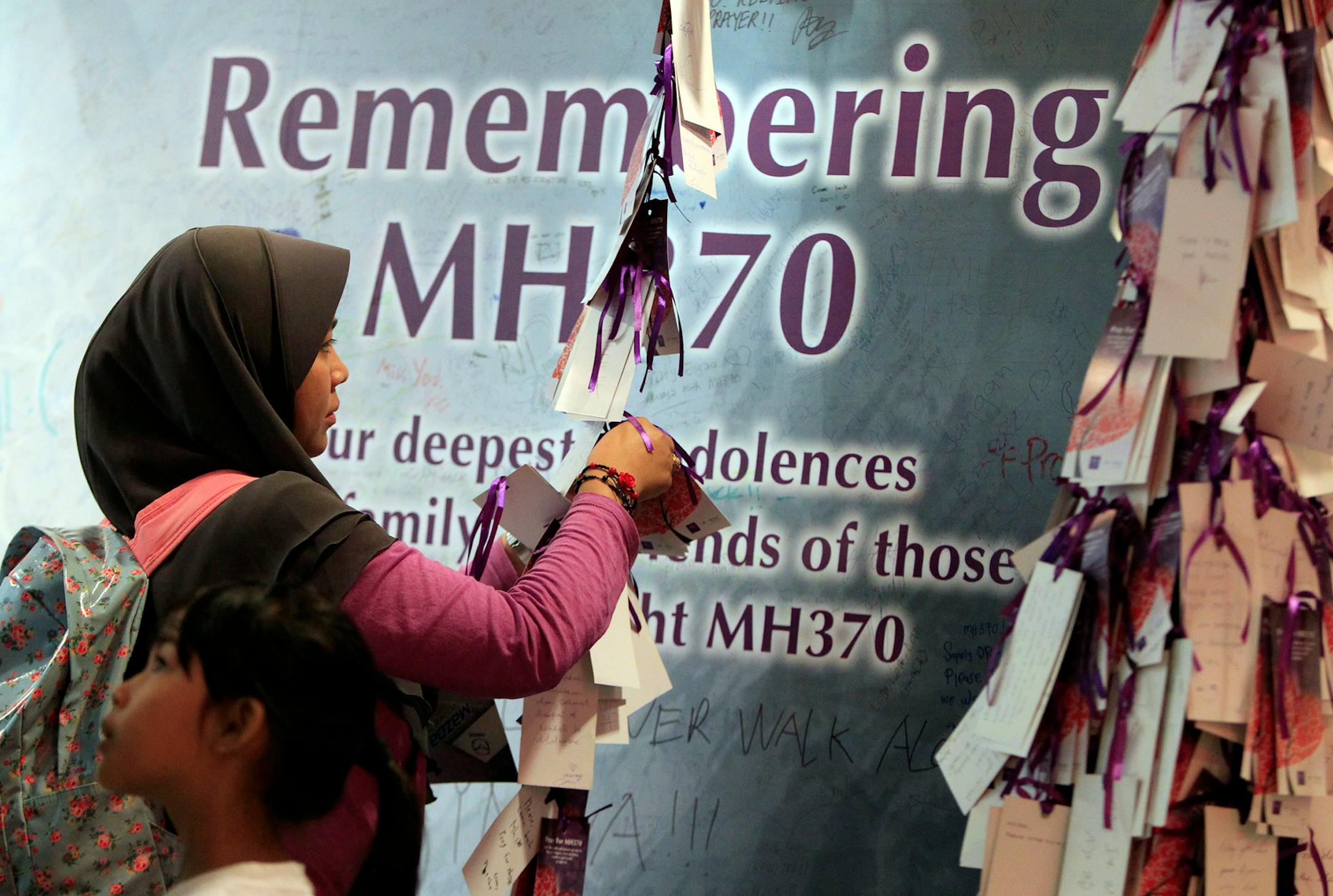 A woman ties a message card for passengers aboard the missing Malaysia Airlines flight MH370, at a shopping mall in Kuala Lumpur, Malaysia, Saturday, April 5, 2014. Search teams racing against time to find the flight recorders from the missing Malaysia Airlines jet crisscrossed another patch of the Indian Ocean on Saturday, four weeks to the day after the airliner vanished. (AP Photo/Lai Seng Sin)