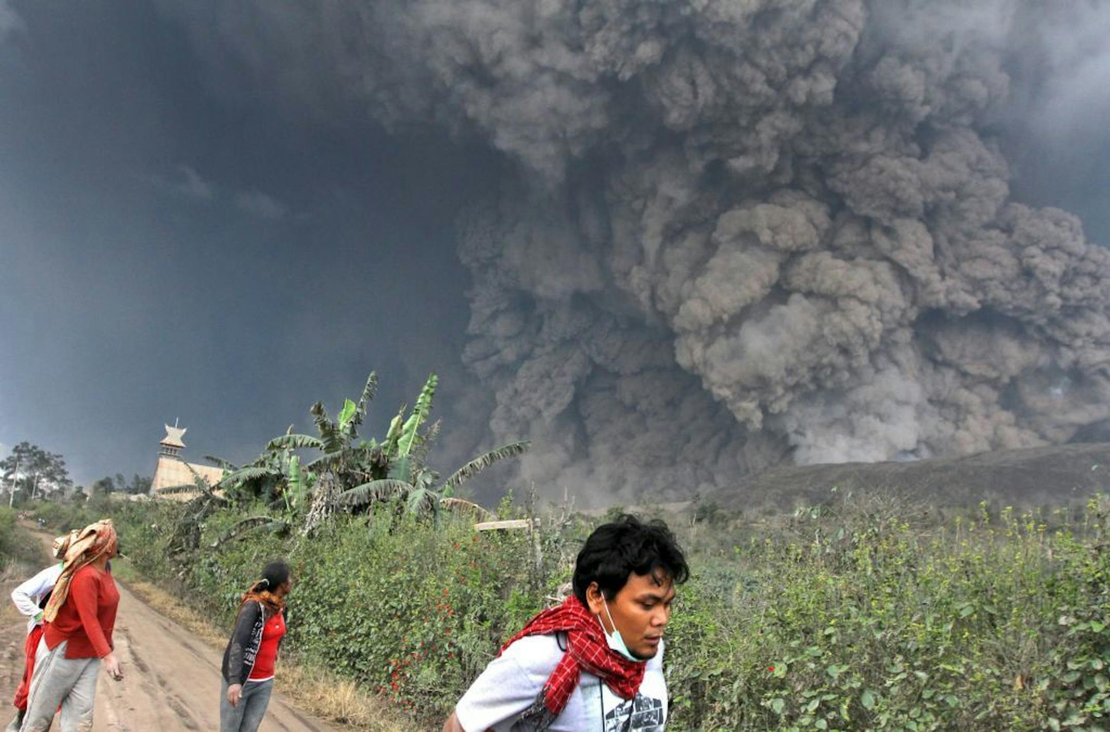 Villagers and a journalist prepare to flee as Mount Sinabung releases pyroclastic flows during an eruption in Namantaran, North Sumatra, Indonesia, Saturday, Feb. 1, 2014.