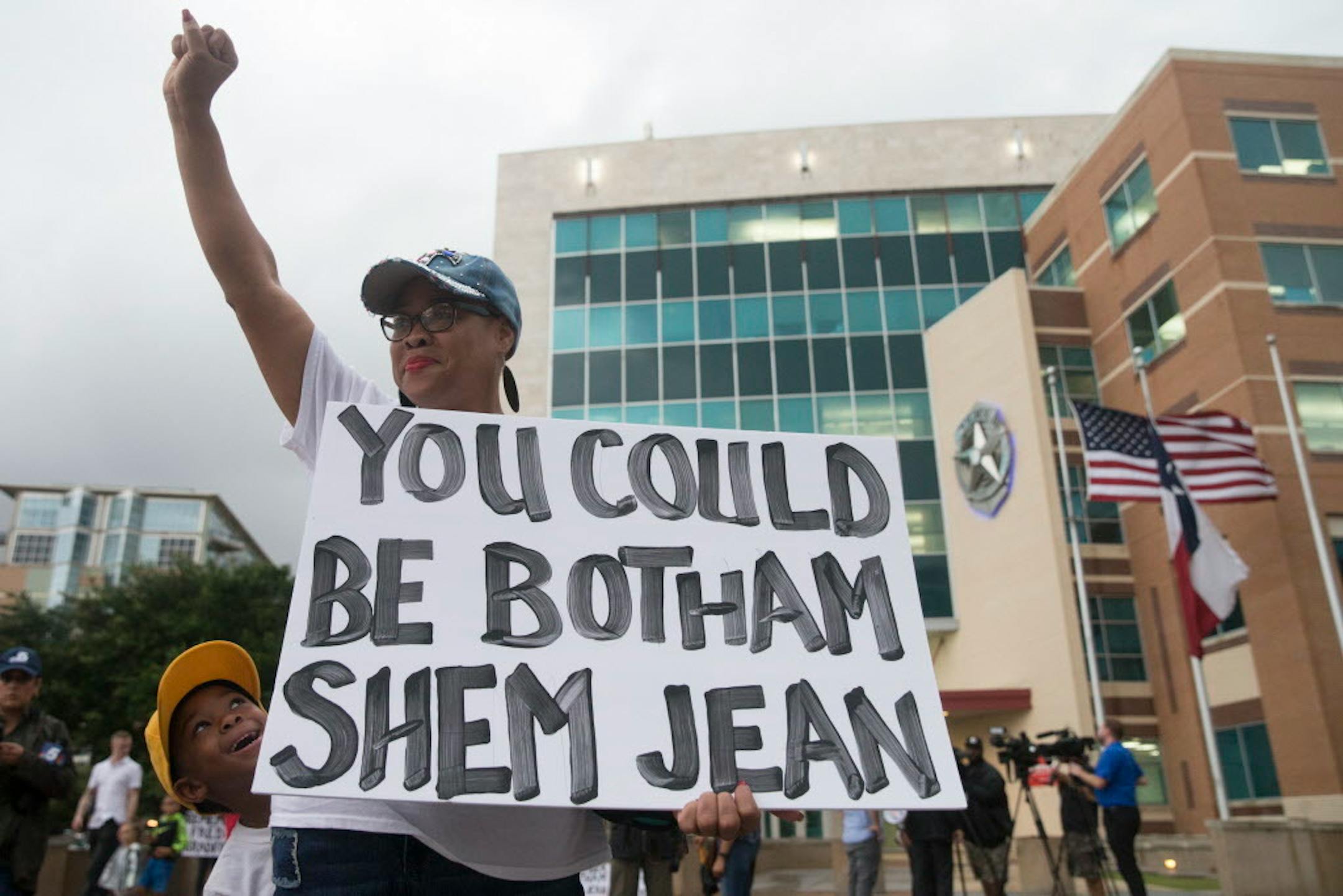 Dr. Pamela Grayson raises her fist as "Young King" Solomon Grayson, 6, peaks behind her sign during a Mothers Against Police Brutality candlelight vigil for Botham Jean at the Jack Evans Police Headquarters on Friday, Sept. 7, 2018, in Dallas. Authorities are seeking a manslaughter warrant for the Dallas police officer who shot and killed Jean after she said she mistook his apartment for her own, police said Friday.