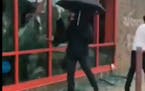 A still from a video shows a man with an umbrella and gas mask breaking windows at the AutoZone on Lake Street during protests in the wake of George F