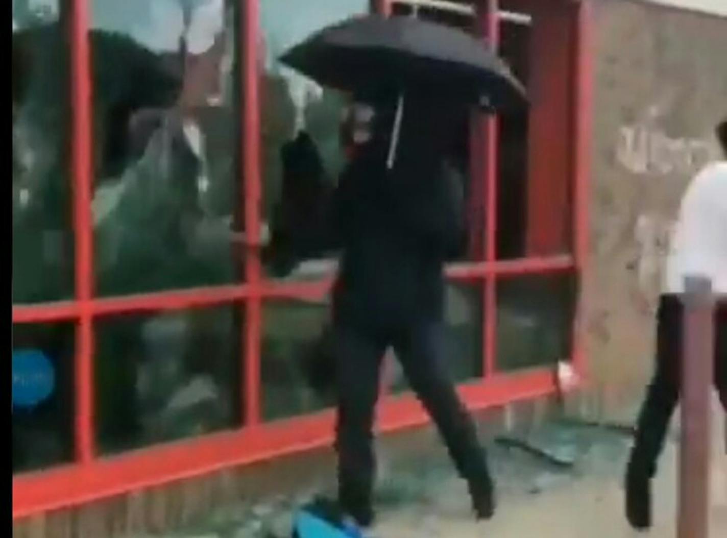 A still from a video shows a man with an umbrella and gas mask breaking windows at the AutoZone on Lake Street during protests in the wake of George Floyd's death. (Twitter/Javier Morillo)