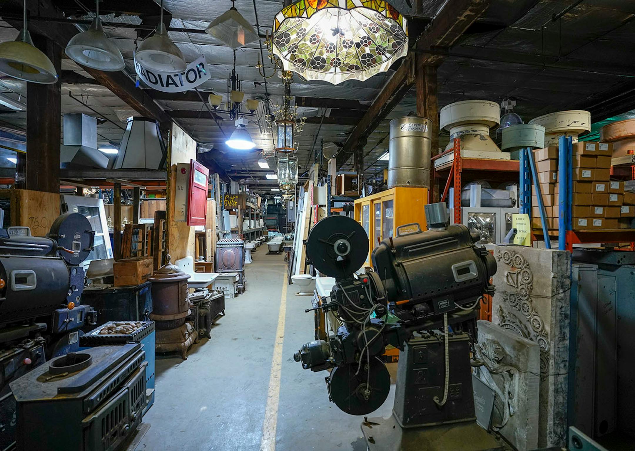 Two movie projectors from Northrup Auditorium sits next to old wood stoves and antique lighting.
