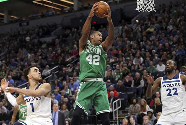 Boston Celtics's Al Horford, center, of Dominican Republic, pulls in a rebound as Minnesota Timberwolves' Tyus Jones, left, and Andrew Wiggins, right,