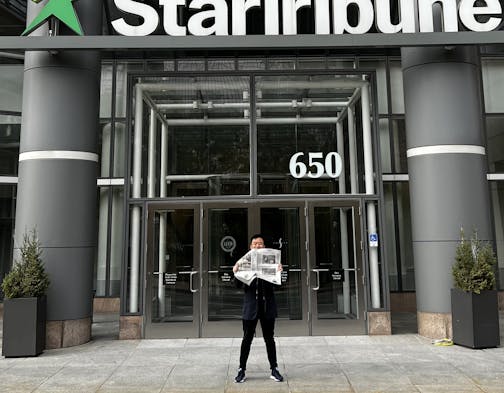 Jon Cheng standing in front of the Star Tribune's downtown Minneapolis office holding a paper with his debut restaurant review.