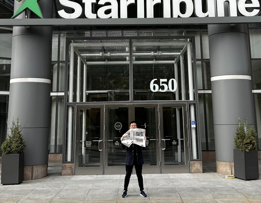 Jon Cheng standing in front of the Star Tribune's downtown Minneapolis office holding a paper with his debut restaurant review.