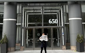 Jon Cheng standing in front of the Star Tribune's downtown Minneapolis office holding a paper with his debut restaurant review.