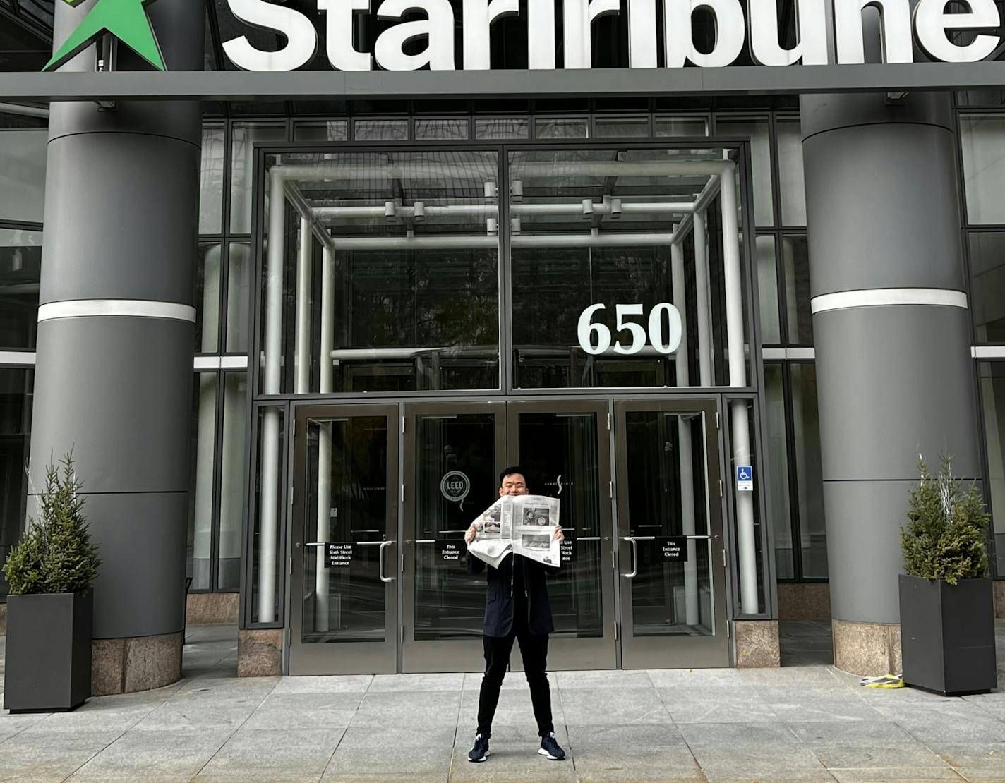 Jon Cheng standing in front of the Star Tribune's downtown Minneapolis office holding a paper with his debut restaurant review.