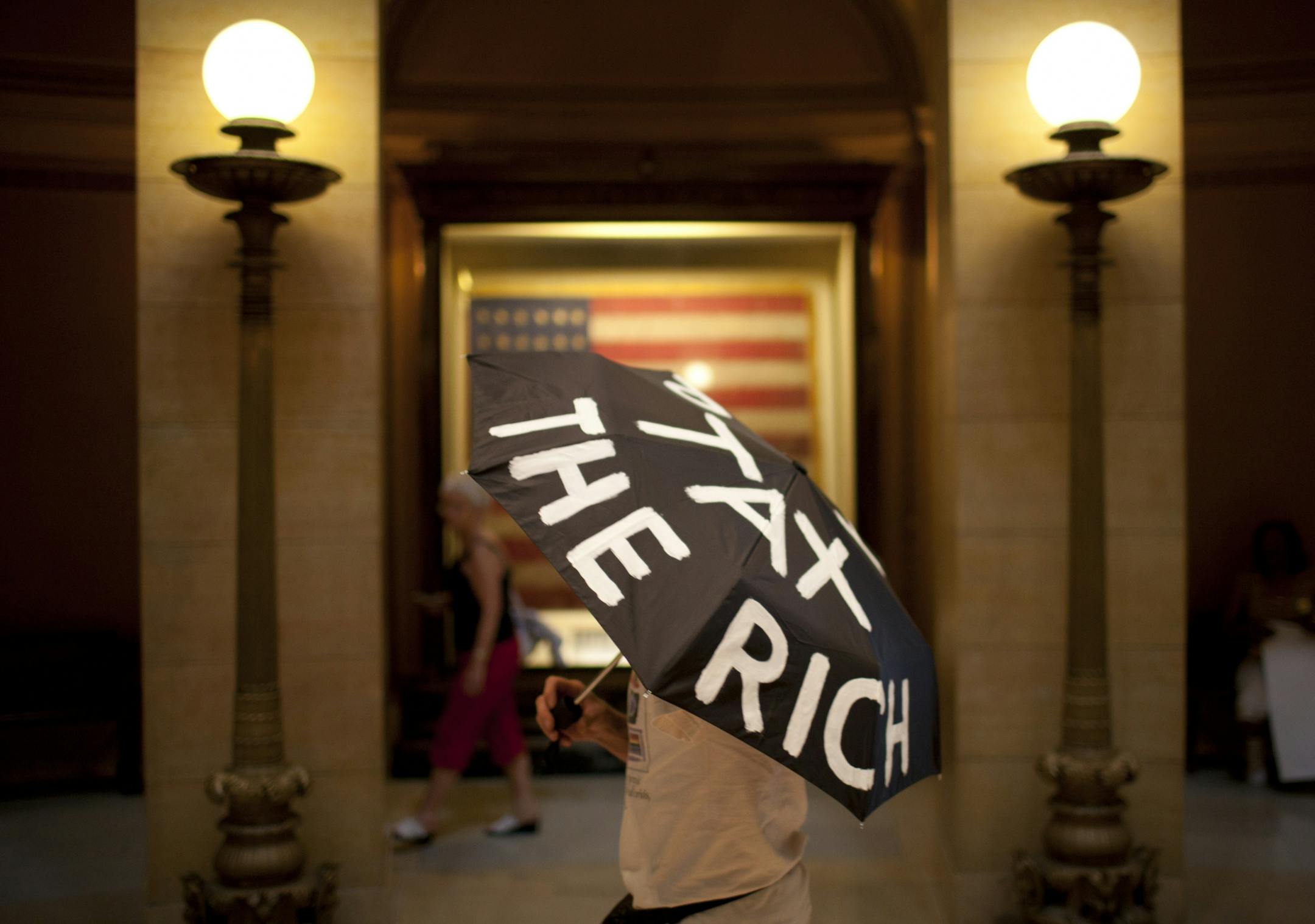 After marching with a small group of demonstrators from Kellogg Mall Park to the steps of the State Capitol in St. Paul, MInn., Bruce Berry of Minneapolis strolled in the cool of the Capitol Rotunda Thursday afternoon, June 30, 2011. His umbrella read "Tax the Rich." Protests were planned for the Capitol grounds all day on Thursday, on the eve of the a state government shutdown.