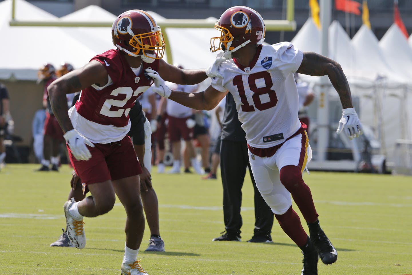 Washington Redskins wide receiver Josh Doctson (18) runs a route in front of cornerback Quinton Dunbar (23) during the NFL football training camp in Richmond, Va., Friday, July 26, 2019. (AP Photo/Steve Helber)