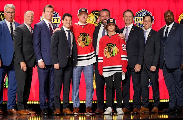 Oliver Moore, center, posed with Blackhawks officials after being taken 19th overall in the NHL draft on Wednesday night in Nashville.