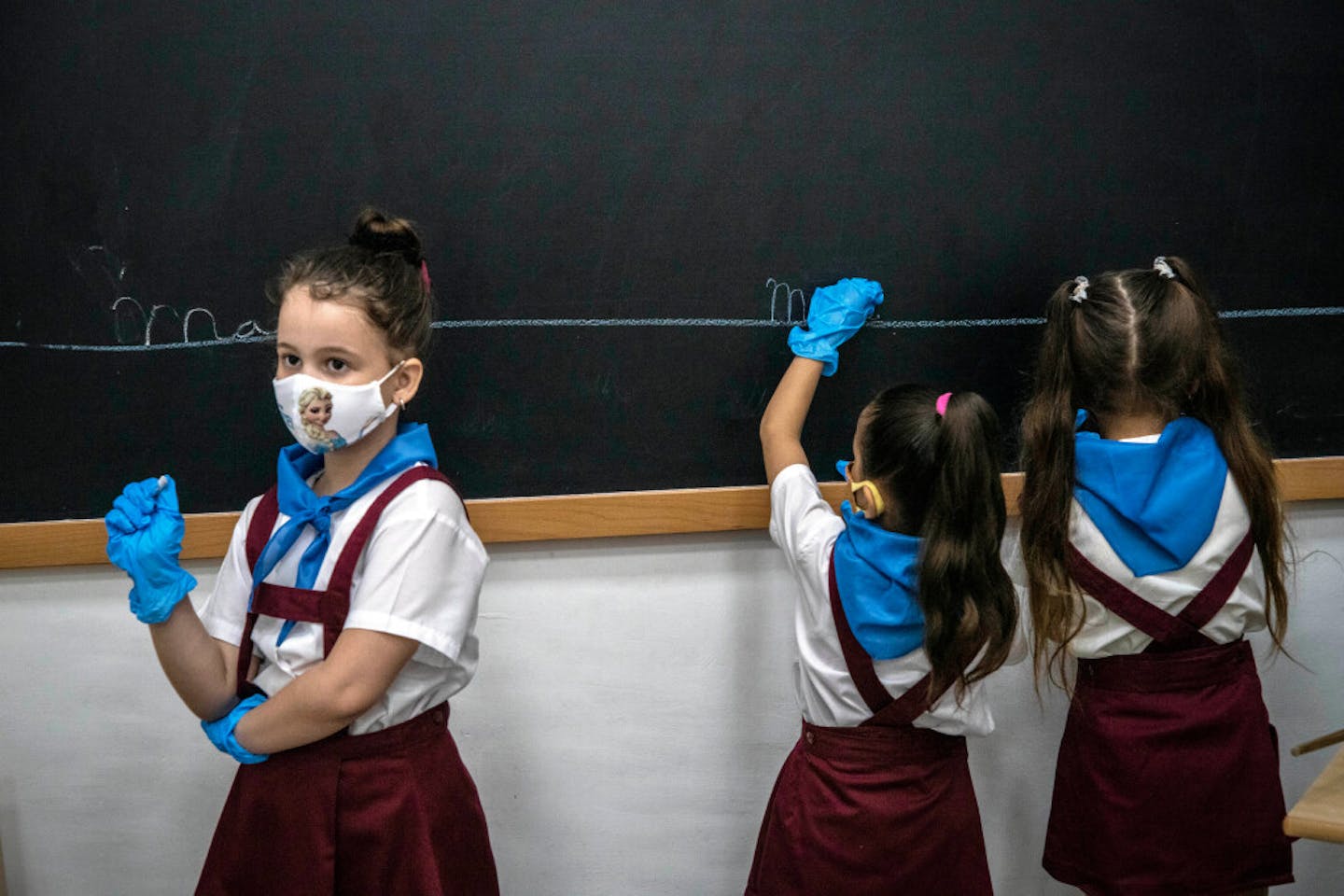 Wearing masks and plastic gloves amid the spread of the new coronavirus, girls write on the chalkboard during class in Havana, Cuba, Monday, Nov. 2, 2020. Tens of thousands of school children returned to class Monday in Havana for the first time since COVID-19 prompted authorities to shut the island down in April.