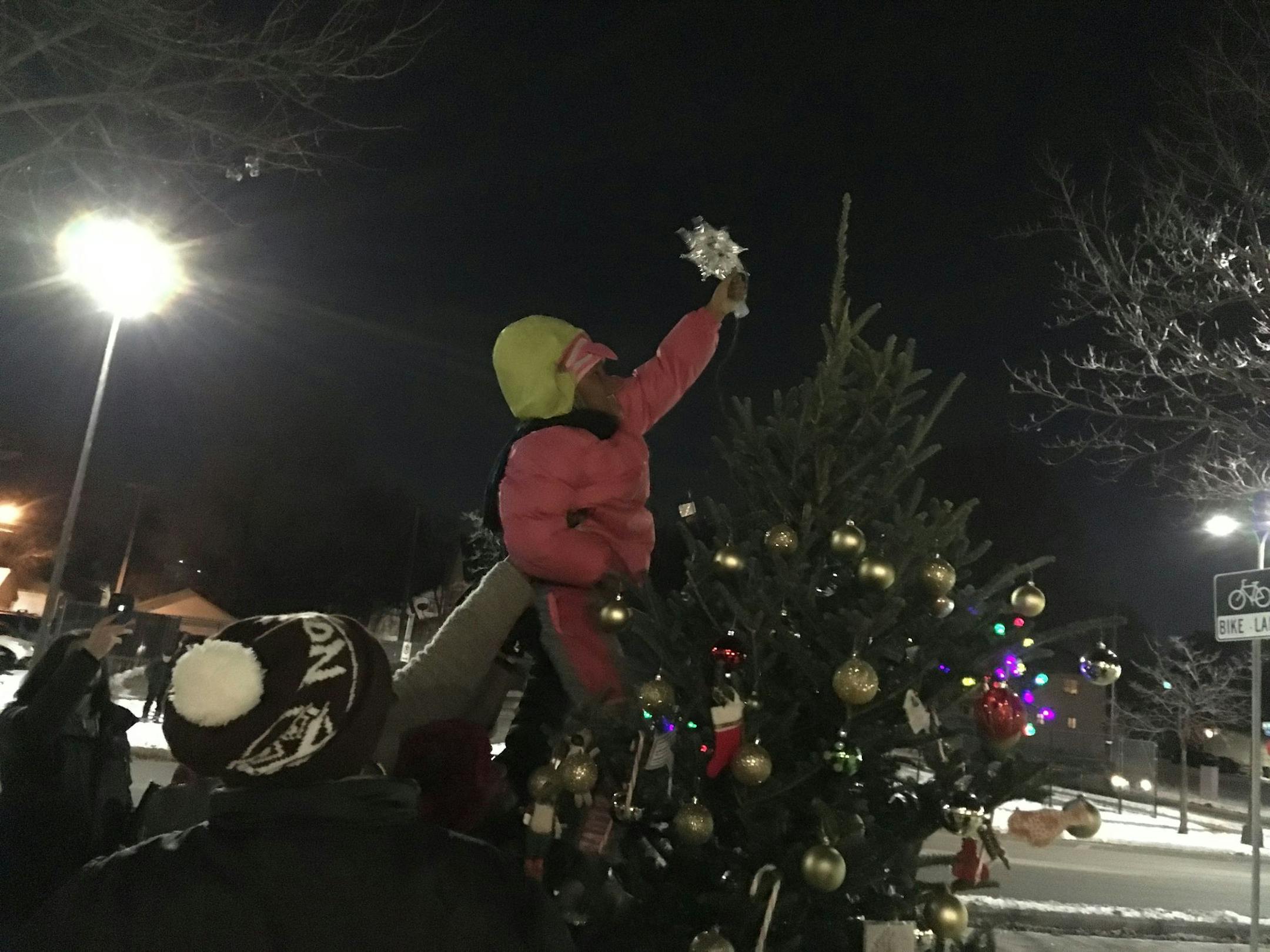 Blessing Caldwell, a first grader from North Minneapolis, gets a boost as she places the star atop the community Christmas tree outside the Fourth Police Precinct. The new tree was a neighborhood response to one in the precinct that officers had decorated with cigarette carton, fast food wrappers and a cup from a fried chicken restaurant.