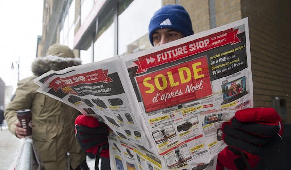 Mahdi Esmaili looks at a flyer offering big discounts as he queues outside an electronics store on Boxing Day in Montreal, Thursday, Dec. 26, 2013. (A