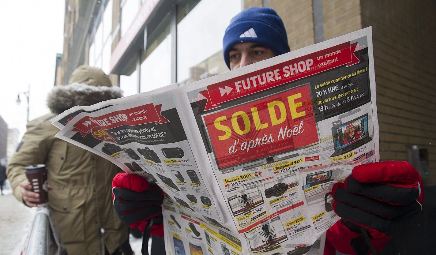 Mahdi Esmaili looks at a flyer offering big discounts as he queues outside an electronics store on Boxing Day in Montreal, Thursday, Dec. 26, 2013. (AP Photo/The Canadian Press, Graham Hughes)