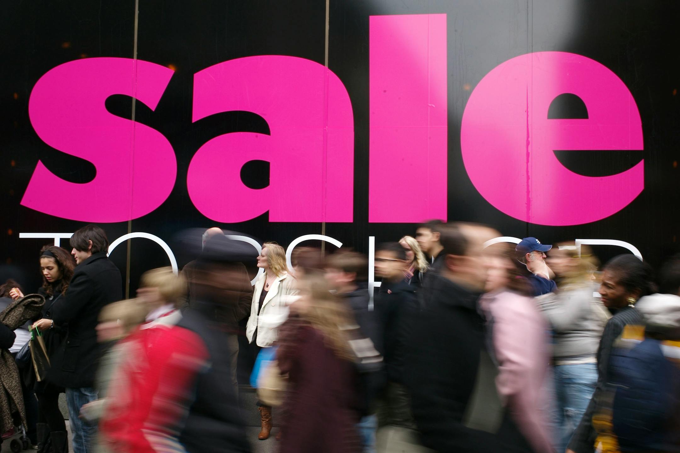 Shoppers walk past a sale sign.
