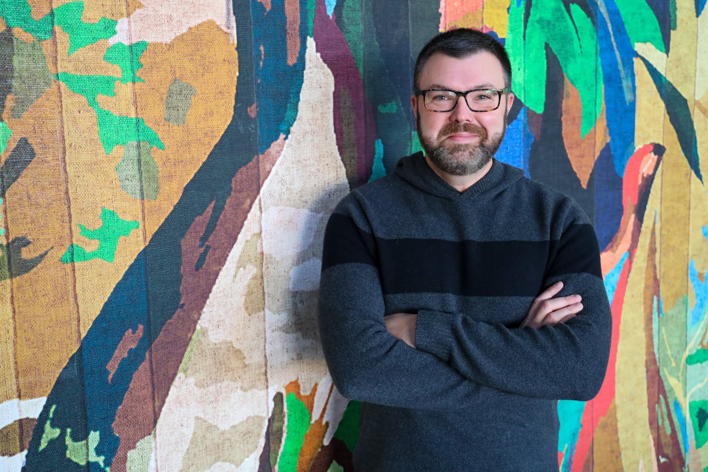 Jason Matheson leans with arms folded in front of him against a colorful tapestry