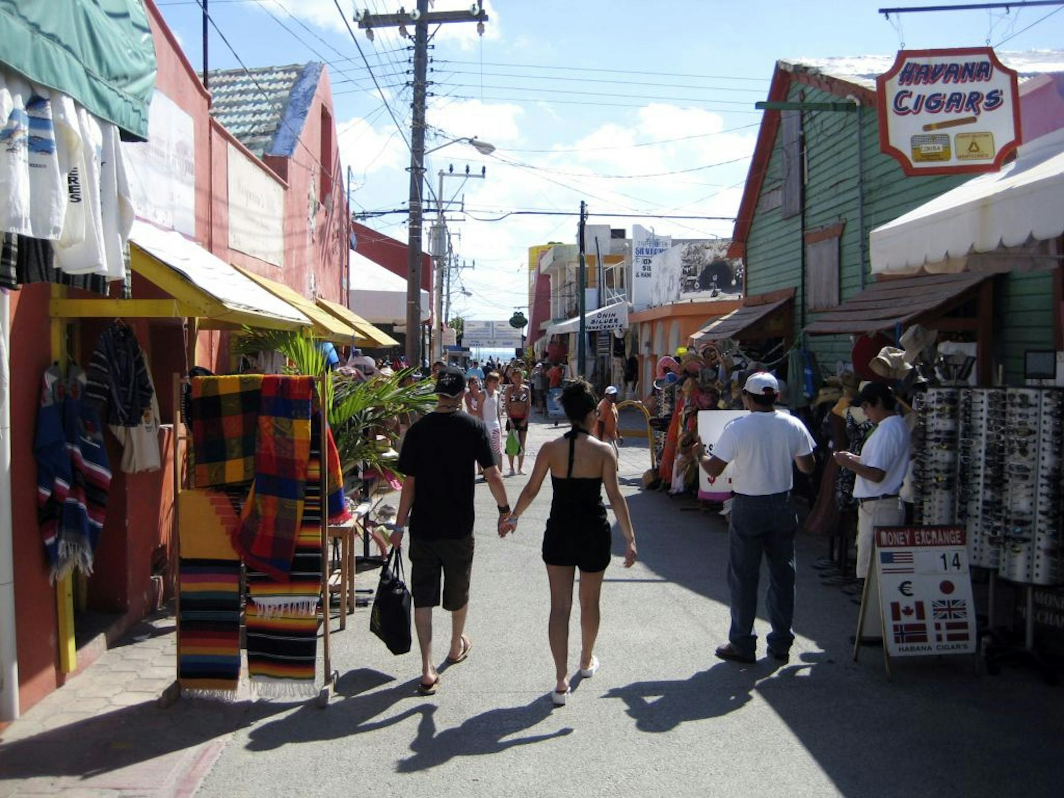 A couple strolls a street lined with small shops on Isla Mujeres, Mexico.