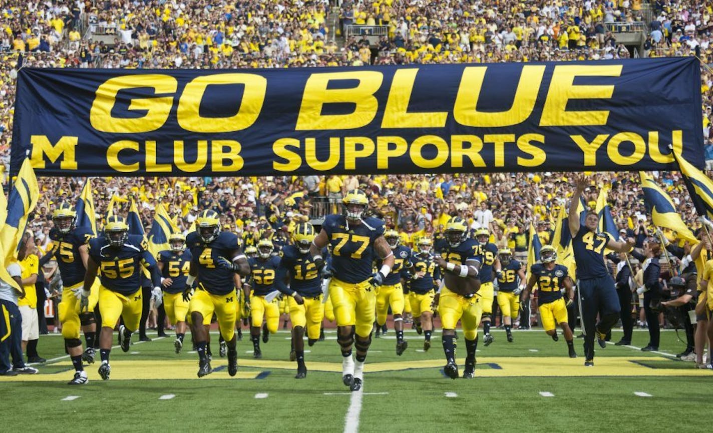 Michigan offensive lineman Taylor Lewan (77) leads his teammates onto the Michigan Stadium field, under the team's traditional "GO BLUE" banner, before an NCAA college football game with Central Michigan, Saturday, Aug. 31, 2013, in Ann Arbor, Mich.