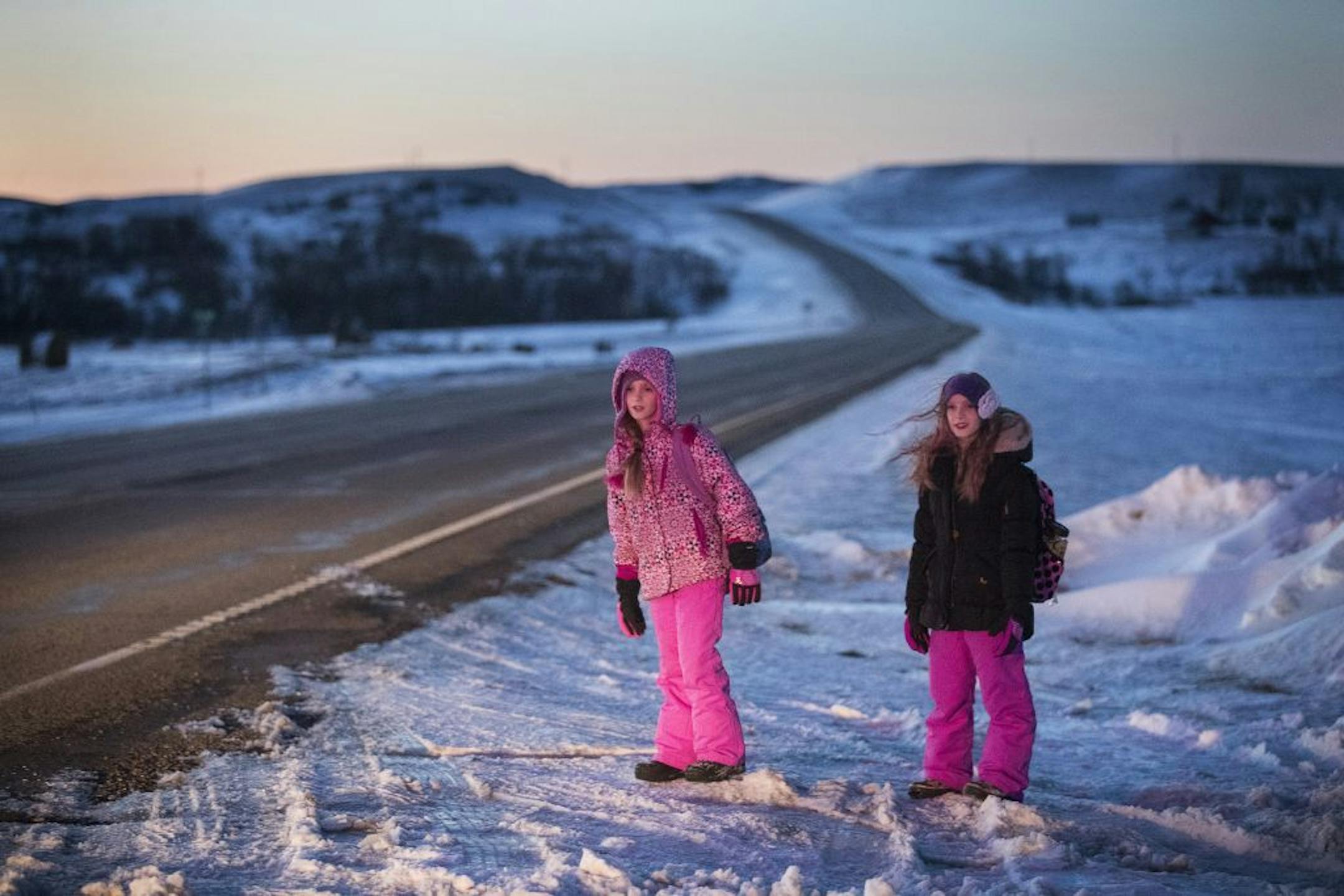 Isabelle, left, and Abby Carlsen wait for the school bus outside their house in the morning.