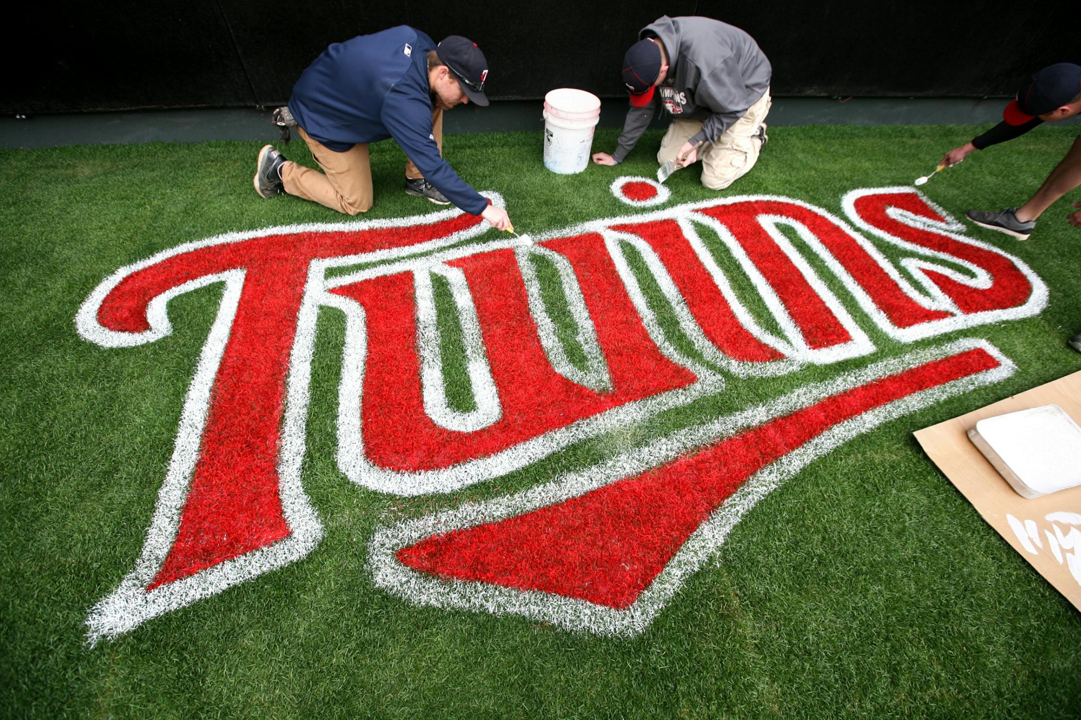 Left to right, Kyle Larson, Jake Hannes and Trenton Waters hand-paint a logo on the grass beneath the batter's eye as the Twins grounds crew prepares Target Field for the home opener April 8, 2012.