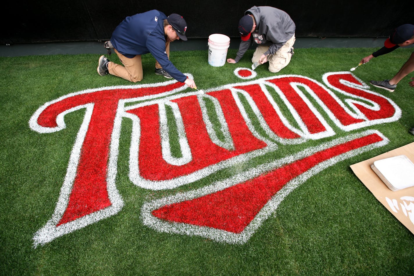 Left to right, Kyle Larson, Jake Hannes and Trenton Waters hand-paint a logo on the grass beneath the batter's eye as the Twins grounds crew prepares Target Field for the home opener April 8, 2012.