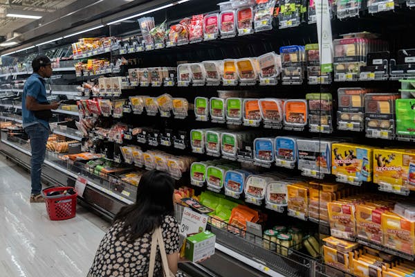 Shoppers in aisle of grocery store check prices of lunch items.