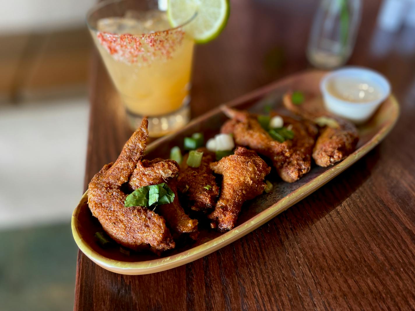 A stoneware plate is lined with crusty fried wings, garnished with sliced green onions and served with a creamy dipping sauce.