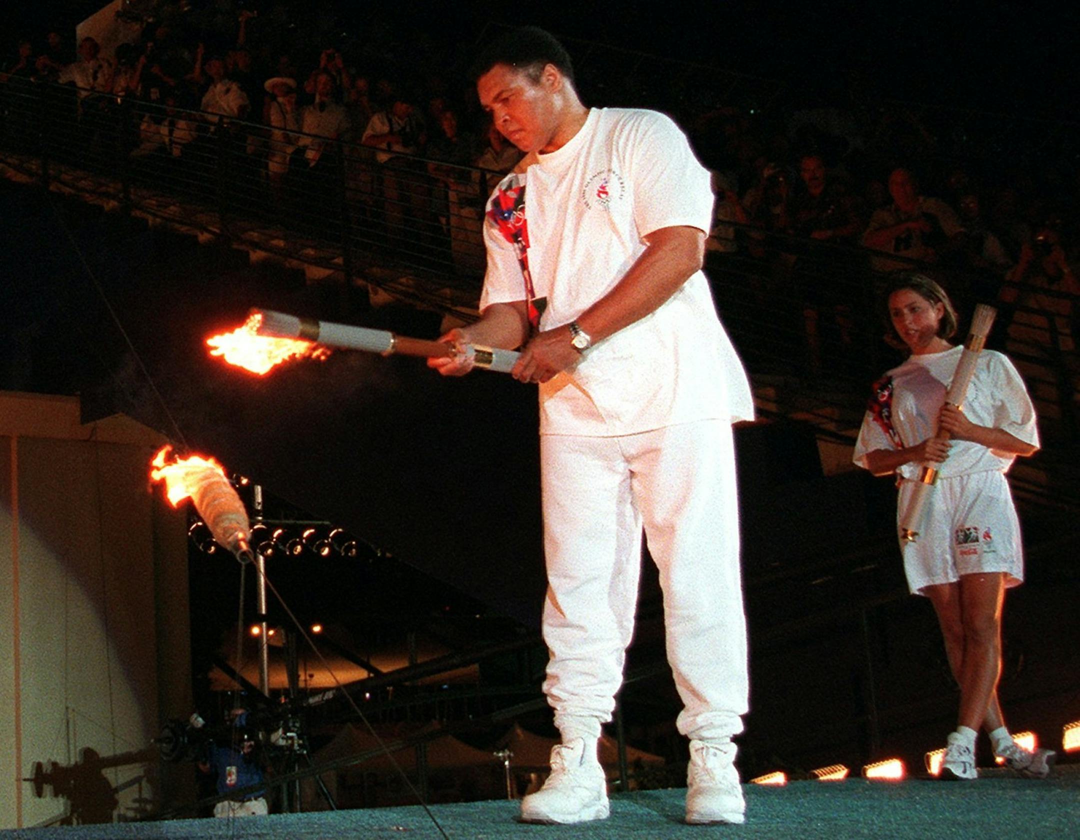 FILE - In this July 19, 1996, file photo, American swimmer Janet Evans looks on as Muhammad Ali lights the Olympic flame during the 1996 Summer Olympic Games opening ceremony in Atlanta. Ali, the magnificent heavyweight champion whose fast fists and irrepressible personality transcended sports and captivated the world, has died according to a statement released by his family Friday, June 3, 2016. He was 74. (AP Photo/Michael Probst, File)