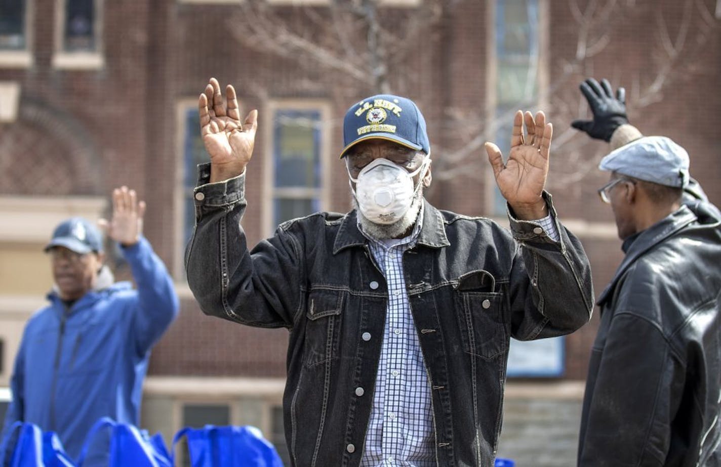 Deacon James Ross and others (center) raised their as the prayed in the parking lot of Greater Mount Vernon Missionary Baptist Church . Five thousands pounds of food was donated through Second Harvest Heartland to help with families dealing with COVID-19 .