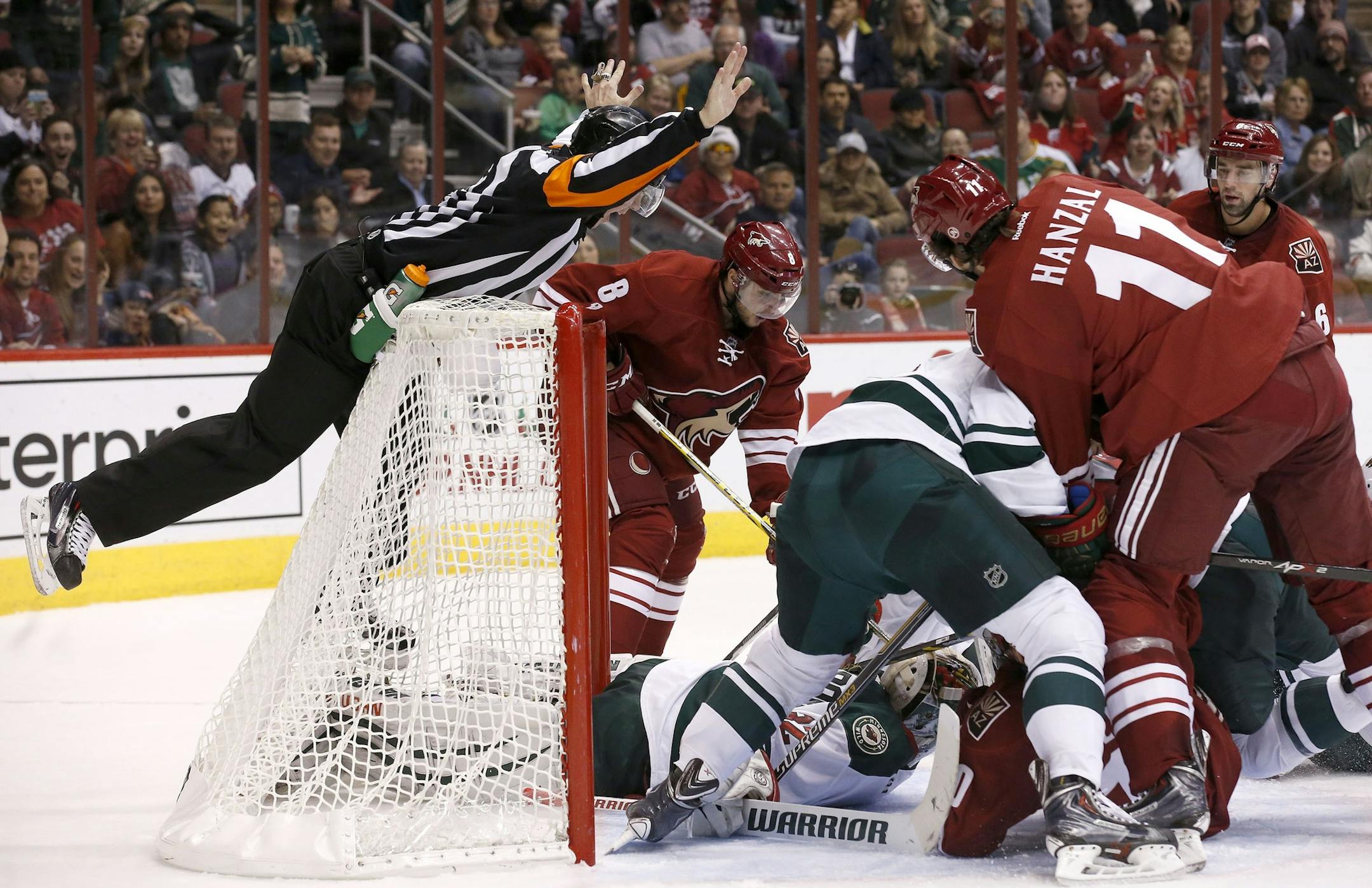 Referee Ian Walsh, left, leaps on the goal as he stops play as Minnesota Wild's Niklas Backstrom (32), of Finland, makes a save as Arizona Coyotes' Martin Hanzal (11), of the Czech Republic, and Tobias Rieder (8), of Germany, wait for the puck to come out during the second period of an NHL hockey game Saturday, Dec. 13, 2014, in Glendale, Ariz. (AP Photo/Ross D. Franklin)