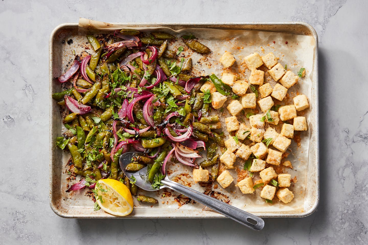 Crispy baked tofu with sugar snap peas in New York, March 28, 2023. A lacy crust of grated Parmesan makes sheet-pan tofu even crispier, Melissa Clark writes. Food styled by Simon Andrews. (Christopher Testani/The New York Times)