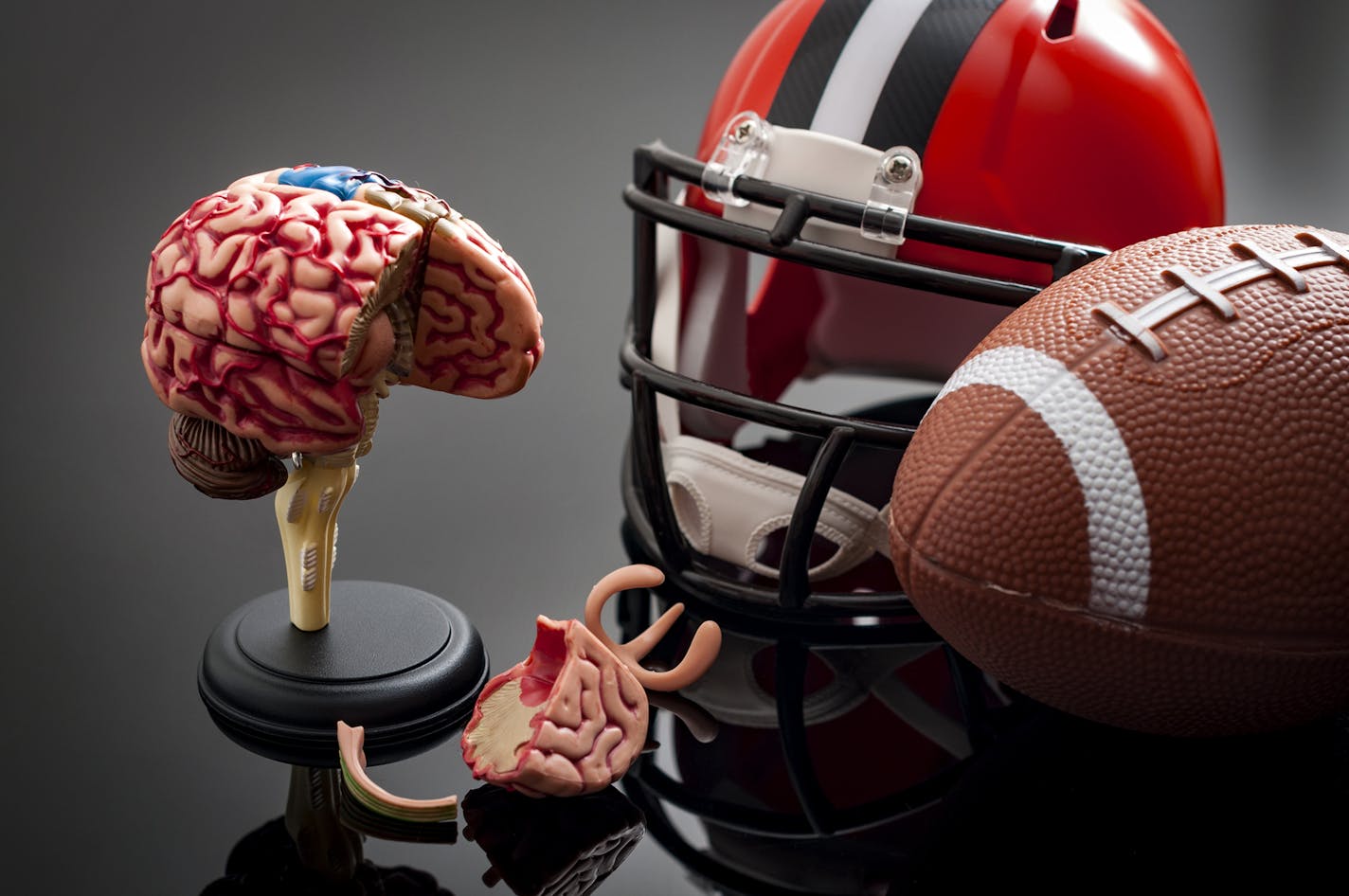 Brain damage and sports injury concept with damaged brain model, american football helmet and a ball, illustrating CTE (Chronic traumatic encephalopathy) a syndrome caused by repeated concussion