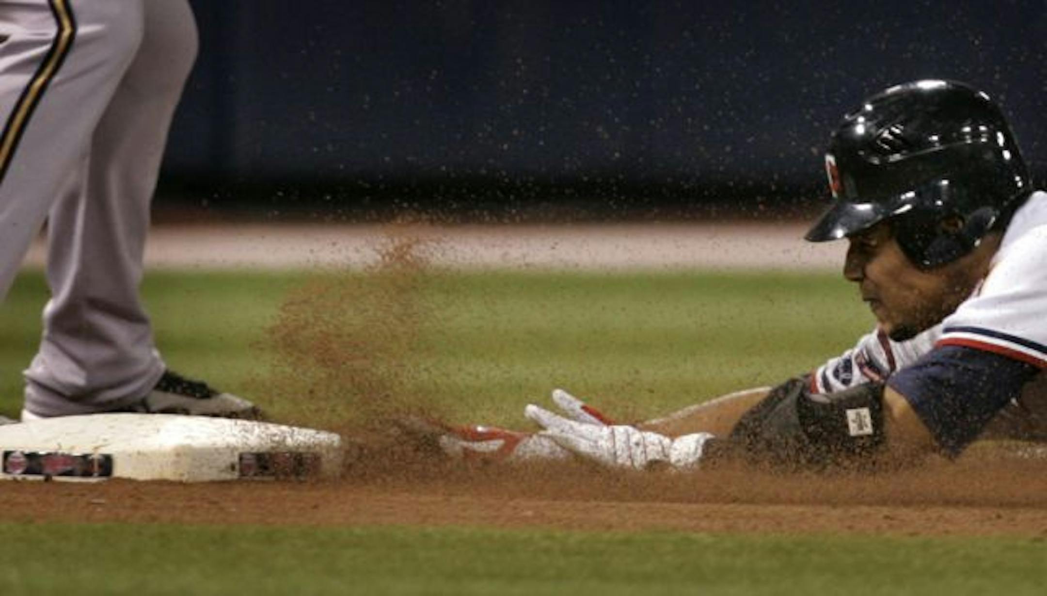 Minnesota Twins center Carlos Gomez slides in safely for a triple, beating the throw to Milwaukee Brewers third baseman Bill Hall during 6th inning action at the Metrodome.