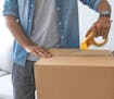 Close up of male hand packing cardboard box, concept moving house. House moving concept. Happy young couple moving into new apartment with packaging b