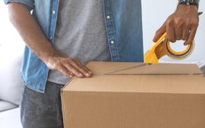 Close up of male hand packing cardboard box, concept moving house. House moving concept. Happy young couple moving into new apartment with packaging b