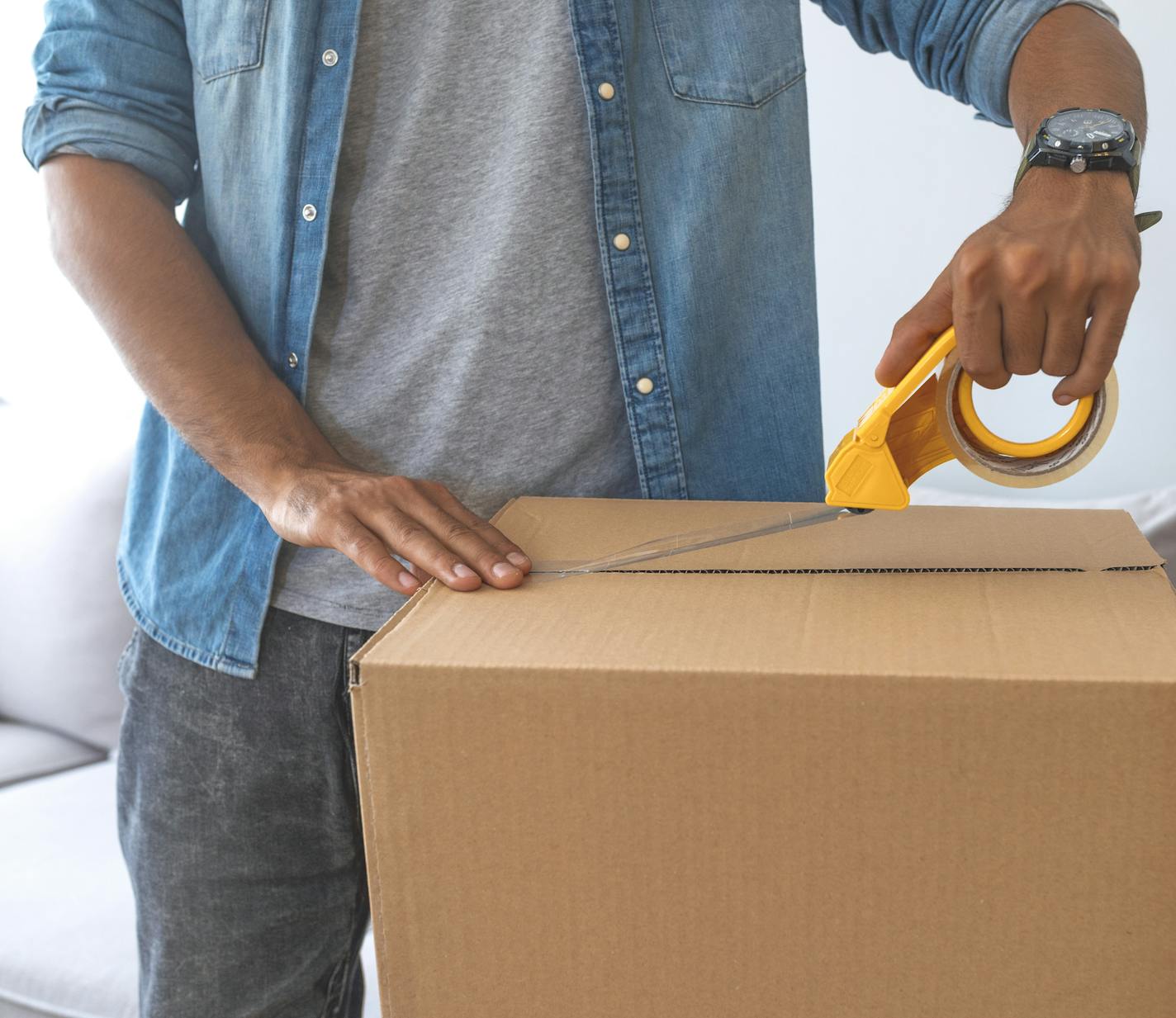 Close up of male hand packing cardboard box, concept moving house. House moving concept. Happy young couple moving into new apartment with packaging boxes. Male hands packing cardboard box with scotch