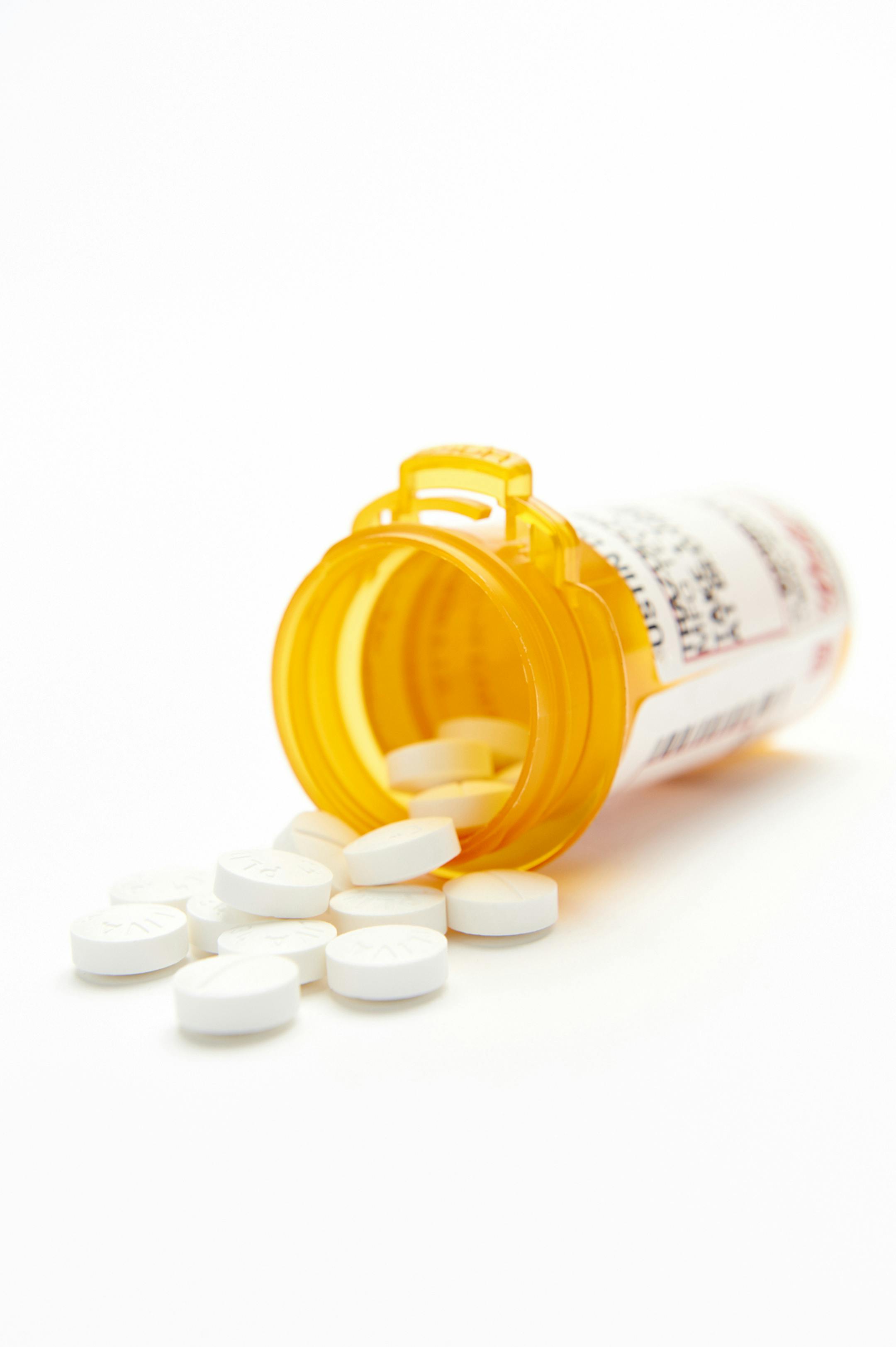 Pill bottle on its side with white round pills spilling out with shallow depth of field and a white backdrop