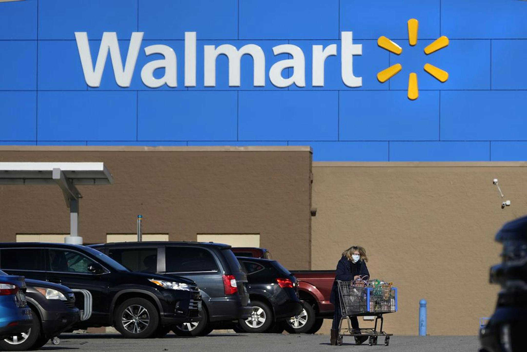 FILE - In this Nov. 18, 2020 file photo, a woman, wearing a protective face mask due to the COVID-19 virus outbreak, wheels a cart with her purchases out of a Walmart store, in Derry, N.H. Shoppers on Walmart.com who pay a $98-a-year membership fee will get free shipping on orders of any size starting Friday, Dec. 4. Walmart announced the membership perk on Wednesday, Dec. 2 doing away with a previous requirement that orders amount to at least $35 to qualify for free shipping.
