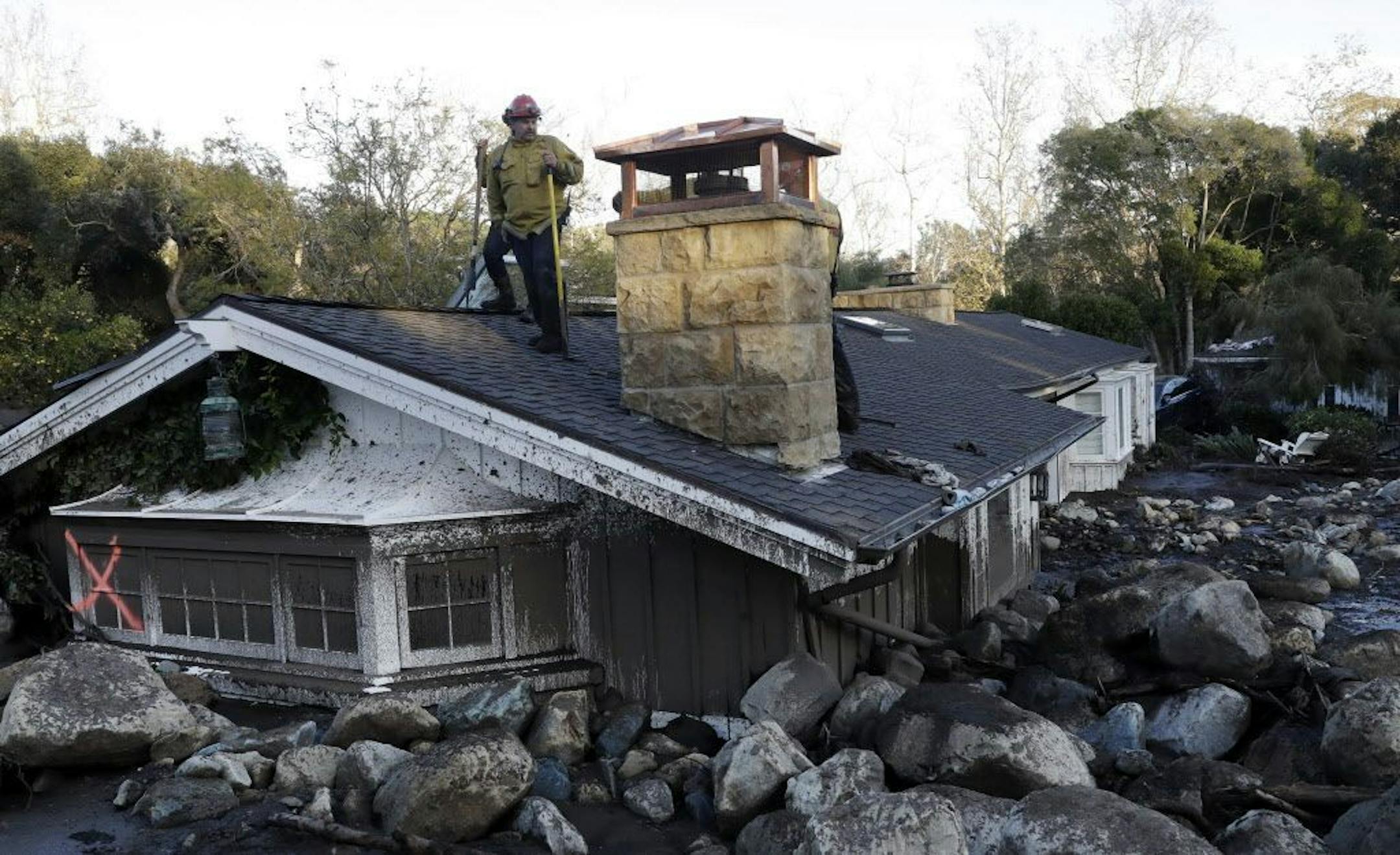 A firefighter stands on the roof of a house submerged in mud and rocks Wednesday, Jan. 10, 2018, in Montecito, Calif. Anxious family members awaited word on loved ones Wednesday as rescue crews searched grimy debris and ruins for more than a dozen people missing after mudslides in Southern California destroyed houses, swept cars to the beach and left more than a dozen victims dead.