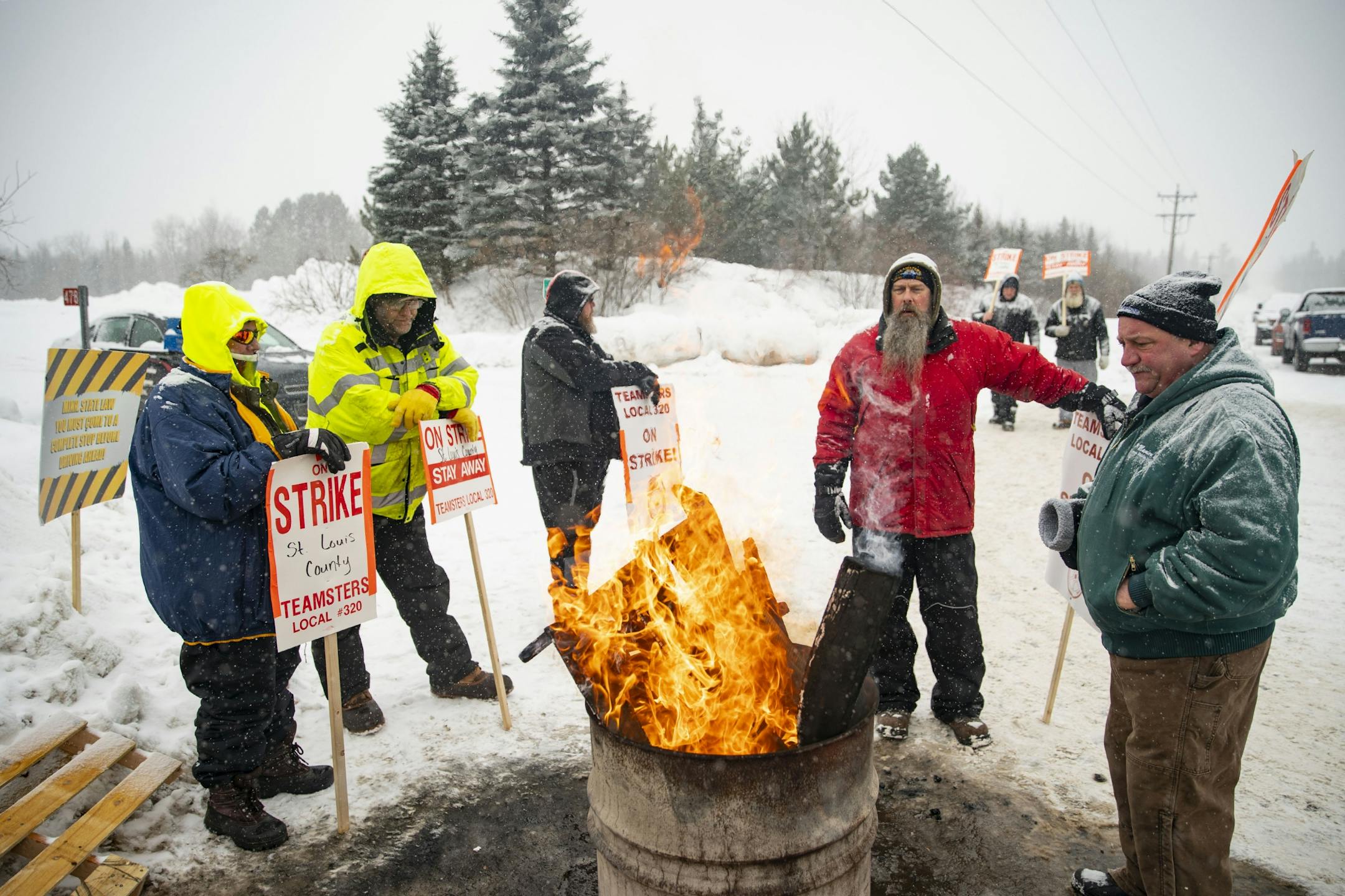 St. Louis County snow plow drivers took a break from picketing ti gather around a small fire in front of the St. Louis County Public Works Department building in Northern Duluth, MN as snow fell on January 15, 2020.
