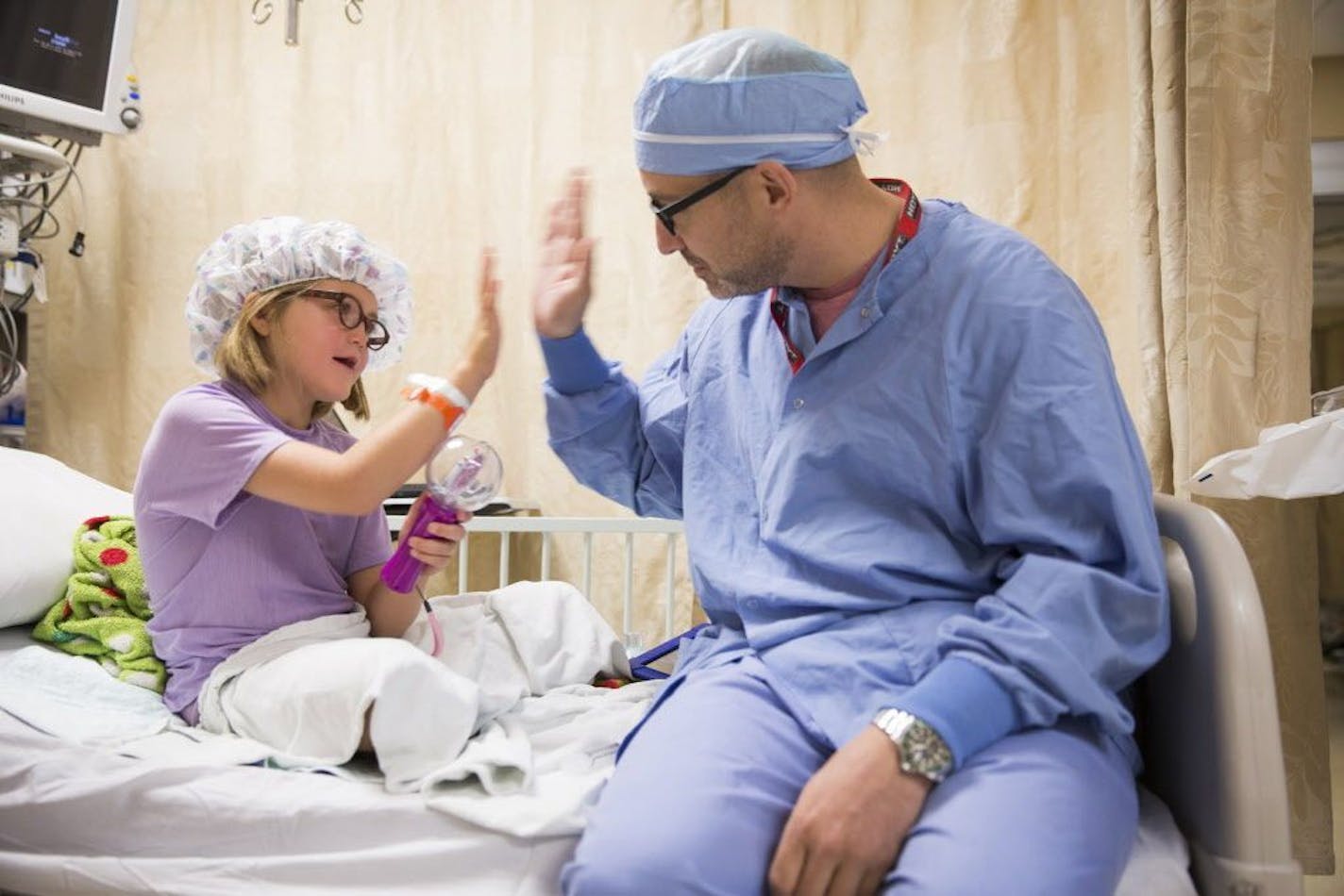 Reagan Lennes, 6, high fives with Lance Svoboda, an oral and maxillofacial surgeon who performed most of her surgeries, before she heads into surgery with another surgeon to fix her left ear at Hennepin County Medical Center in downtown Minneapolis on Tuesday, August 25, 2015.